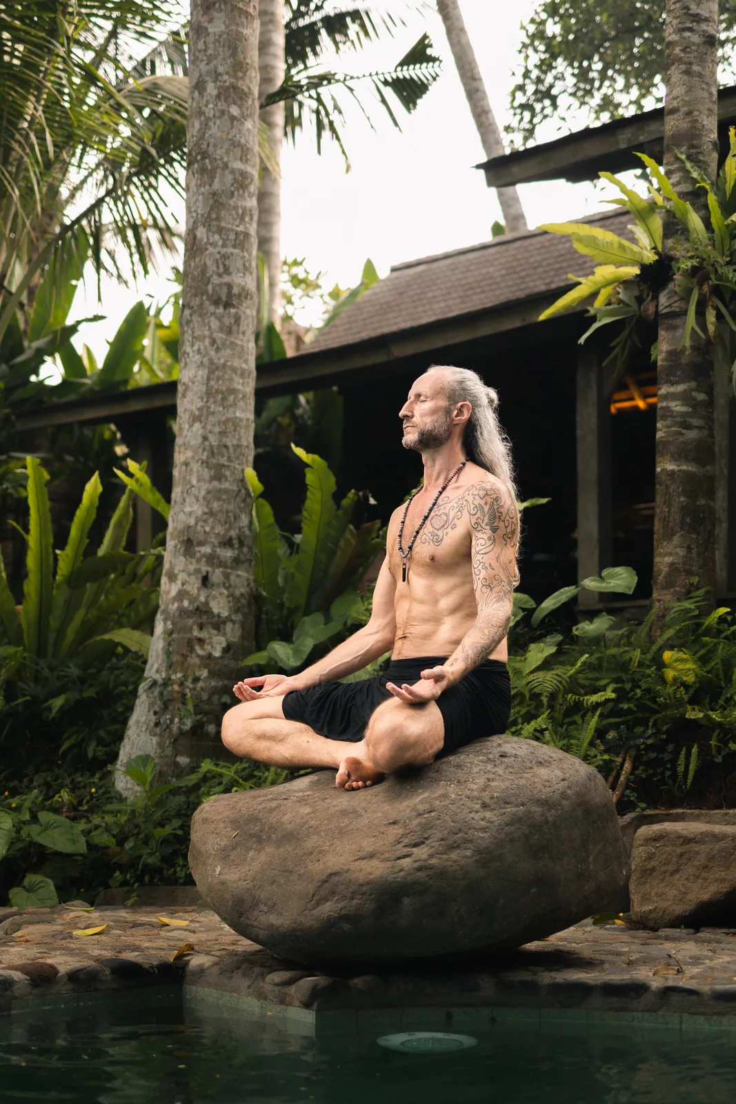 Steve Shiva meditating cross-legged on a rock above a jungle pool in Bali